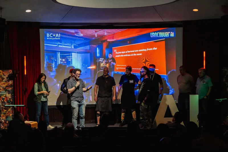 A lineup of presenters onstage in front of a projected demo screen.