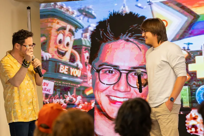 Host handoff and participant presentation beside a projected portrait, photo 172.