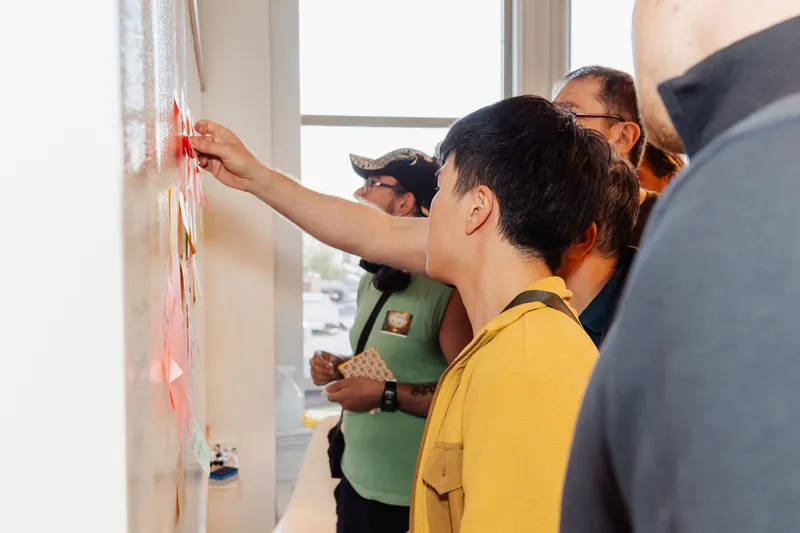 Participants add notes and discuss themes at the idea wall, photo 110.