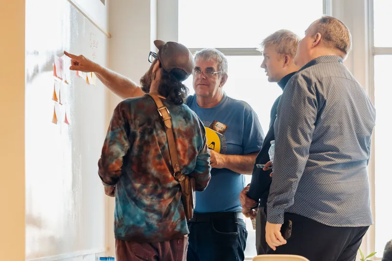 Small groups compare notes beside the collaborative idea wall, photo 090.