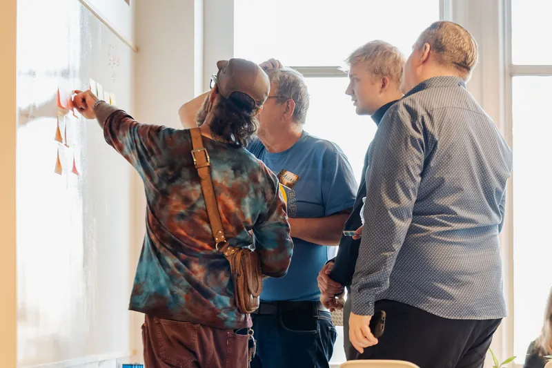 A small group reviews and discusses notes on the idea wall, photo 092.
