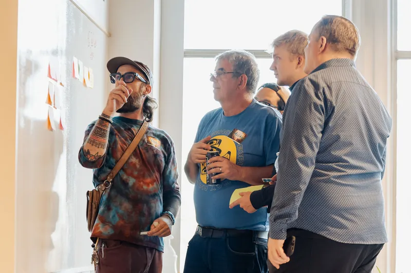 Small groups compare notes beside the collaborative idea wall, photo 093.