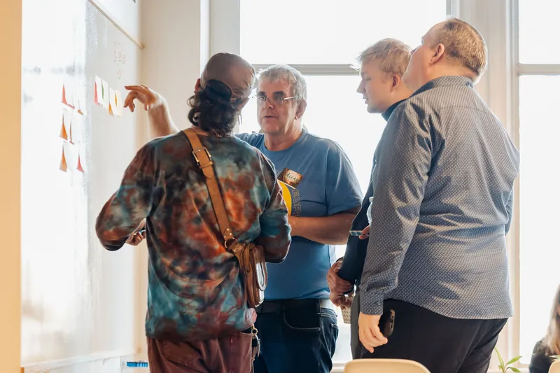 Small groups compare notes beside the collaborative idea wall, photo 091.