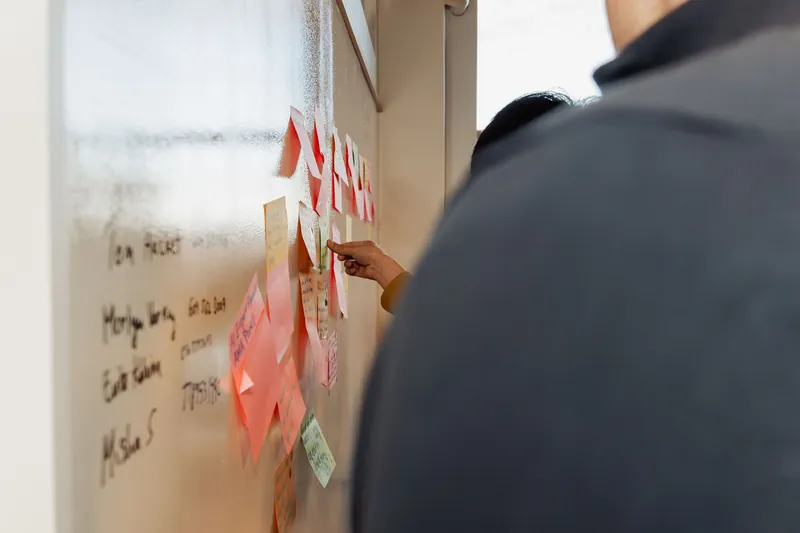 Participants add notes and discuss themes at the idea wall, photo 111.