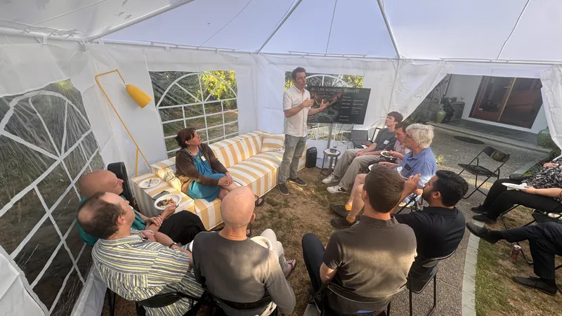A speaker addressing seated guests under the backyard tent.