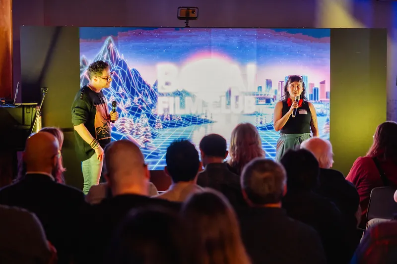 A presenter and audience framed by a large projected AI cityscape.