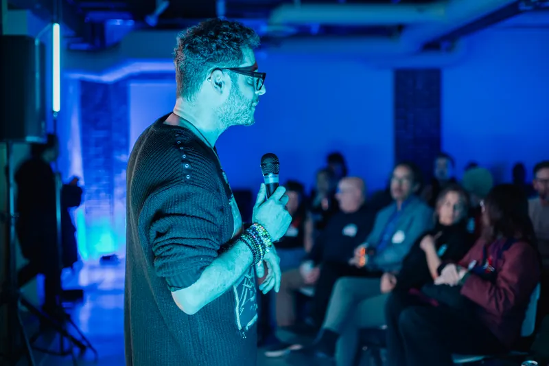 A presenter speaking to the Film Club audience under blue stage light.