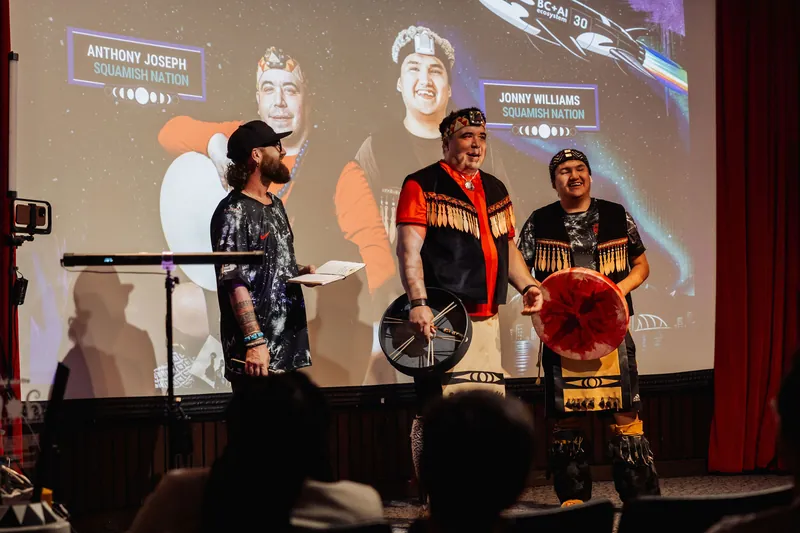 The host and Squamish Nation performers hold the stage as the Vancouver AI wordmark fills the projection behind them.