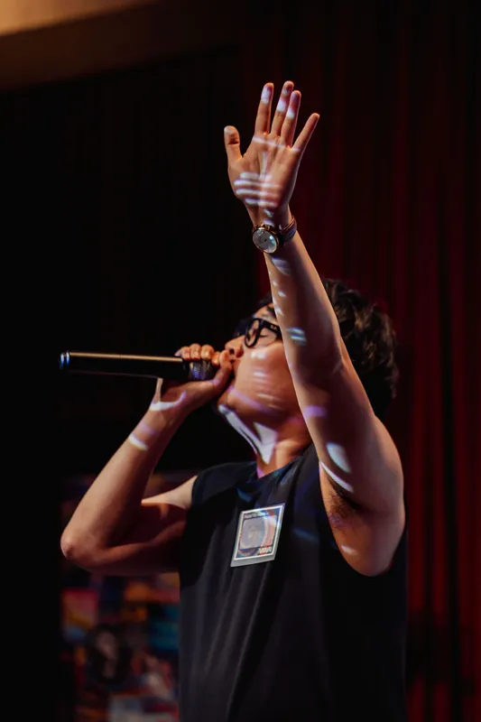The performer reaches skyward with both arms extended, fully absorbed in the moment on stage.