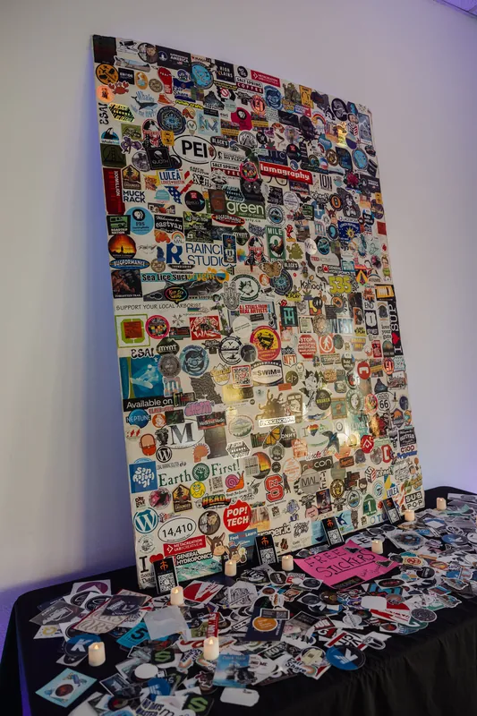 A towering community sticker board anchors the reception table, surrounded by candles and loose stickers.