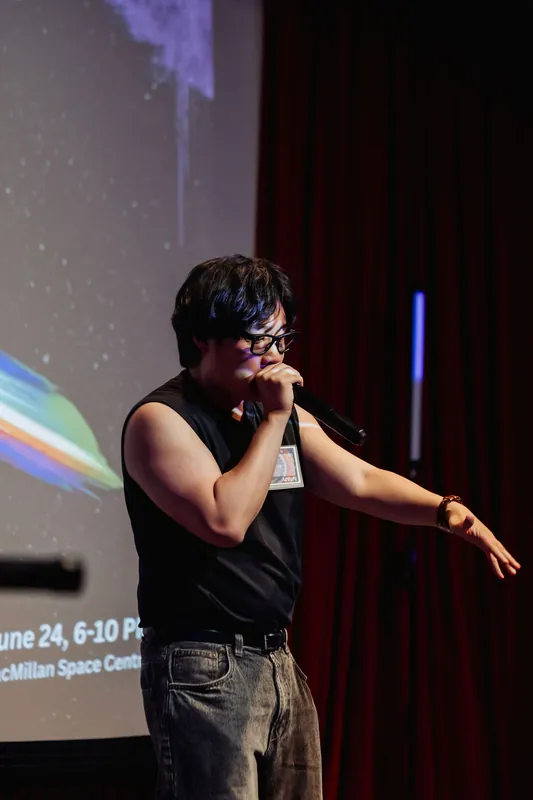 A performer delivers their set beneath the full Vancouver AI Meetup #30 orca-spaceship mission-patch projection.