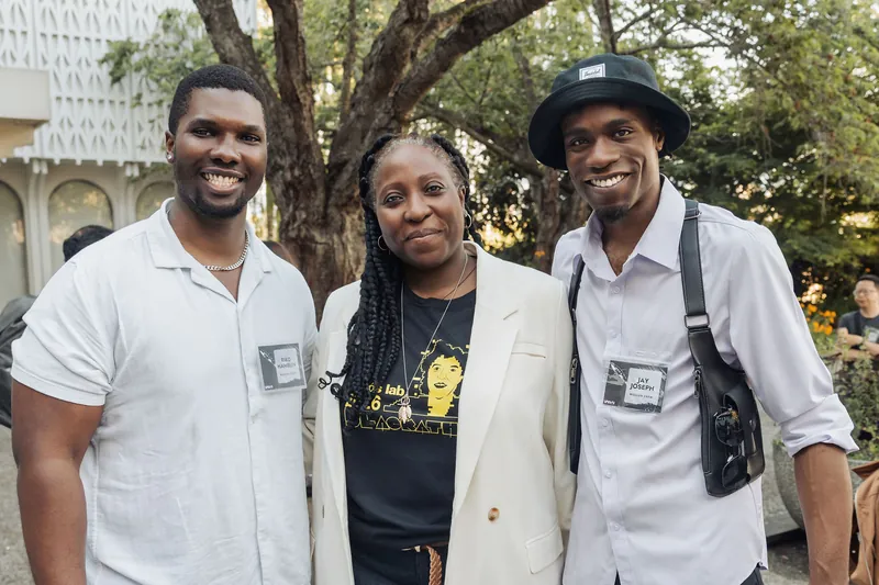Three guests wearing event name badges share a cheerful moment together on the outdoor plaza.