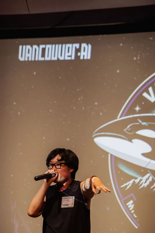 An MC gestures toward the crowd beneath the Vancouver AI mission-patch projection at the Space Centre.