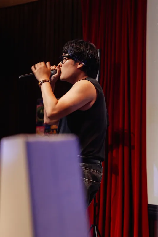 A tight profile captures the performer's intensity as they bring the microphone to their lips against red curtains.