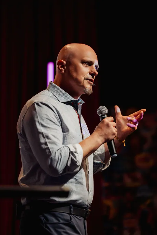 A presenter draws energy into upturned hands mid-talk, the dim stage light catching the conviction in his expression.