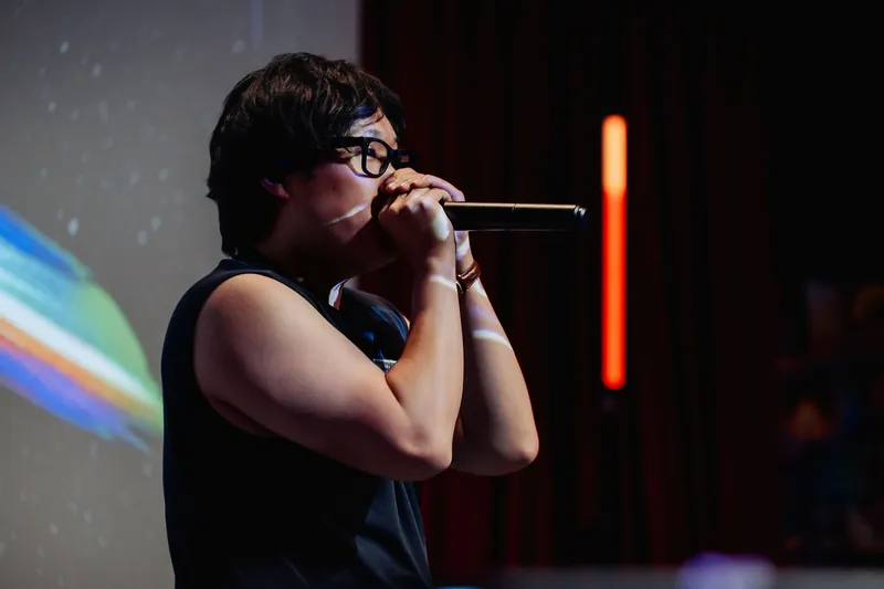 A close portrait of the performer in profile, a spectrum of projection color glowing to the left.
