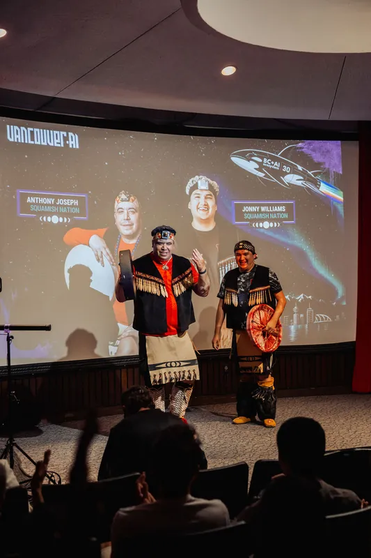 Two Squamish Nation performers step into the spotlight as the Vancouver AI Meetup #30 slide announces their welcome.