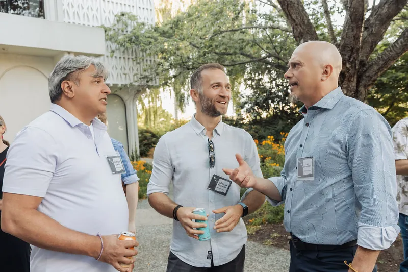 Three attendees share an animated outdoor conversation beside the Space Centre's distinctive white arched facade.
