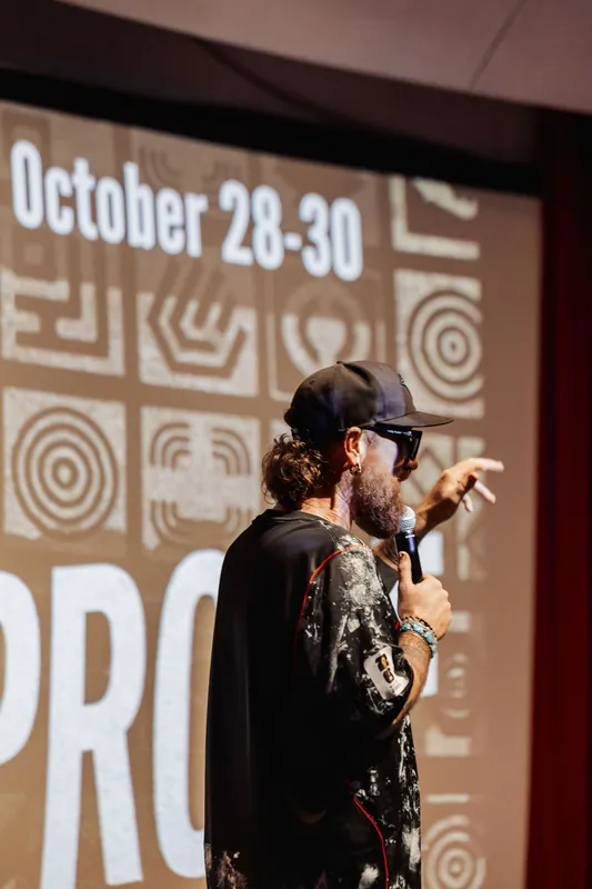 Seen from behind, a speaker gestures upward toward an October event announcement slide projected large in the Space Centre theater.