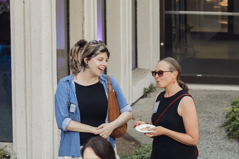 Two attendees share a warm laugh outside the Space Centre's columned facade as the reception hums around them.