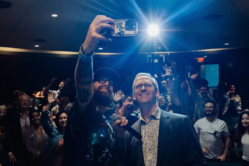 Smiling faces and raised hands fill the hall as the emcee and speaker face the crowd for the shot.