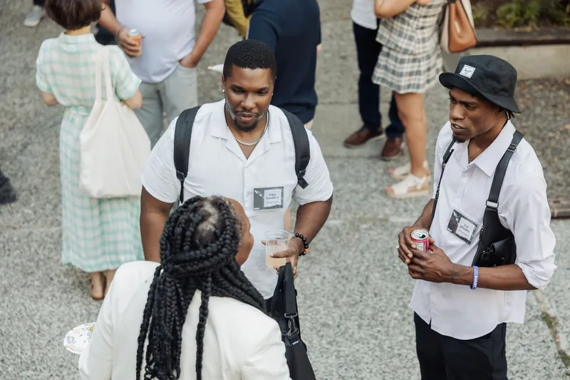Three attendees exchange greetings and drinks during the pre-program outdoor reception on the plaza.