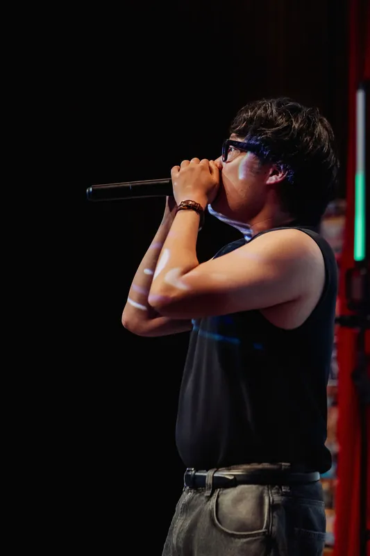 Hands wrapped around the mic, the performer pulls inward for a quiet, concentrated moment.