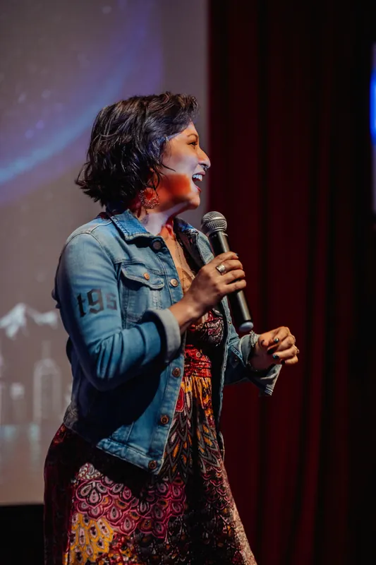 Mayumi Rollins of Tiny Ghost Studios speaks against a cosmic projection.