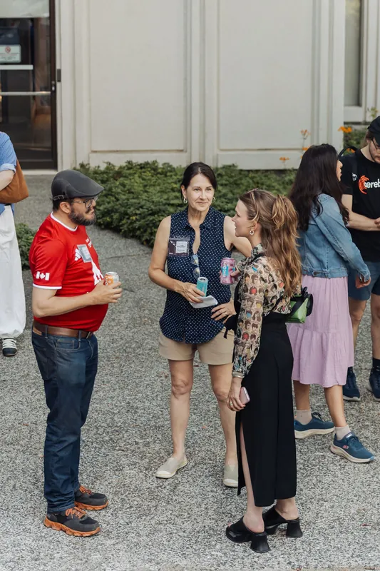 Three attendees chat on the gravel plaza outside the Space Centre's entrance, drinks in hand, at the start of the evening reception.