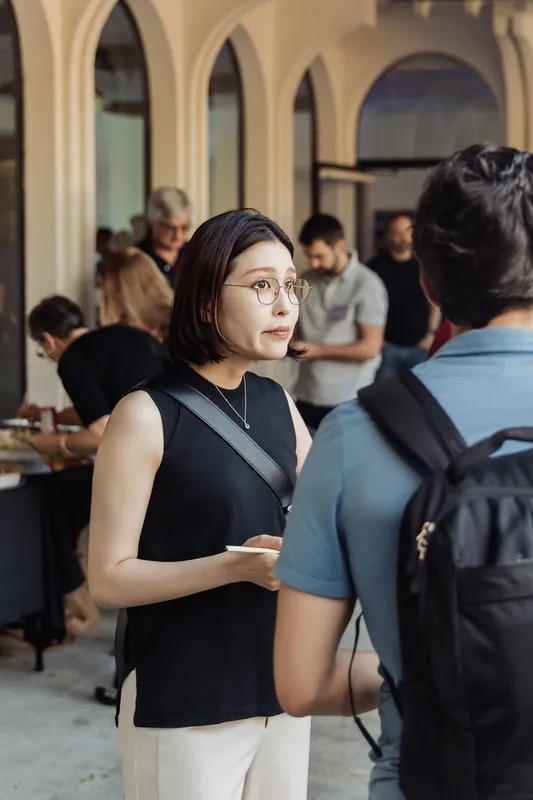An attendee with wire-frame glasses listens intently mid-conversation, small plate in hand, inside the Space Centre's arched lobby during the opening reception.