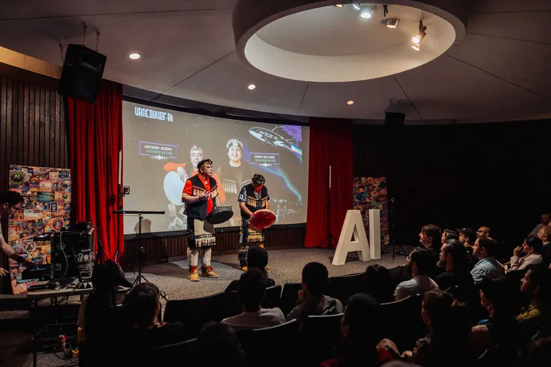Two Squamish Nation drummers are introduced on stage as the Vancouver AI Meetup 30 projection glows behind them.