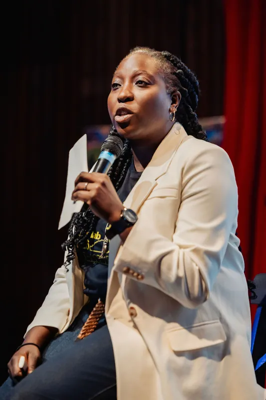 Anthonia Ogundele speaks from her stool on the darkened stage, notes in hand and mic held close.