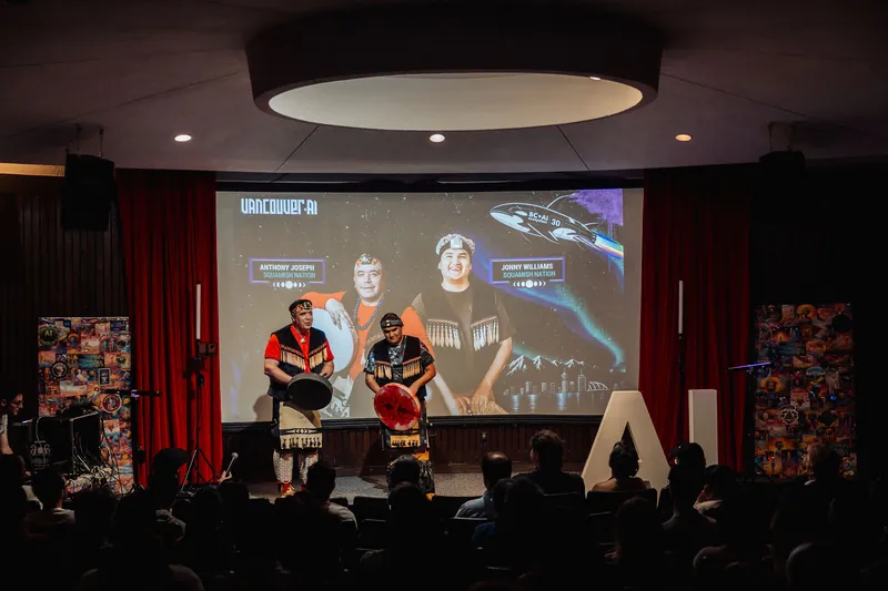 A wider frame takes in the full stage and attentive audience gathered in the warmly lit Space Centre theatre.