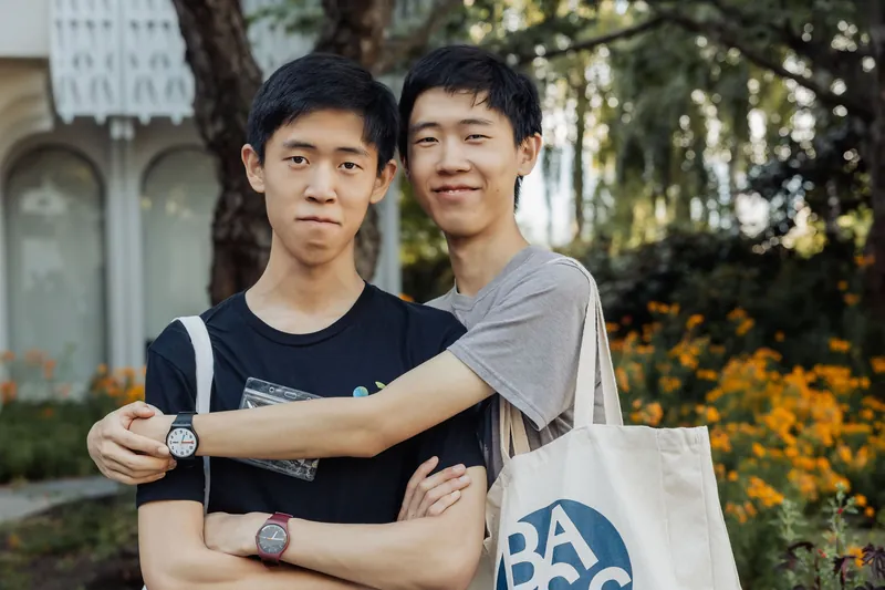 Two friends pose arm-in-arm outside, one proudly carrying a BC AI canvas tote bag.