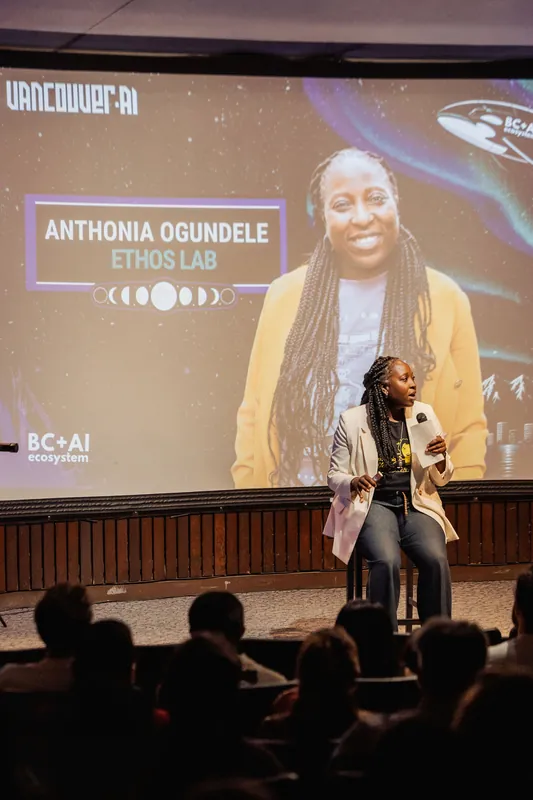 A wide shot shows Anthonia Ogundele of Ethos Lab on stage, her speaker slide projected large above the audience.