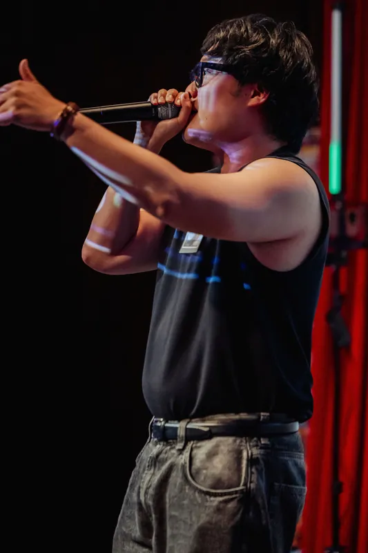 The performer spreads both arms wide, filling the stage with physicality during the indoor program.