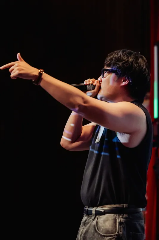A pointed gesture into the crowd punctuates a charged beat, green LEDs glowing in the wings.