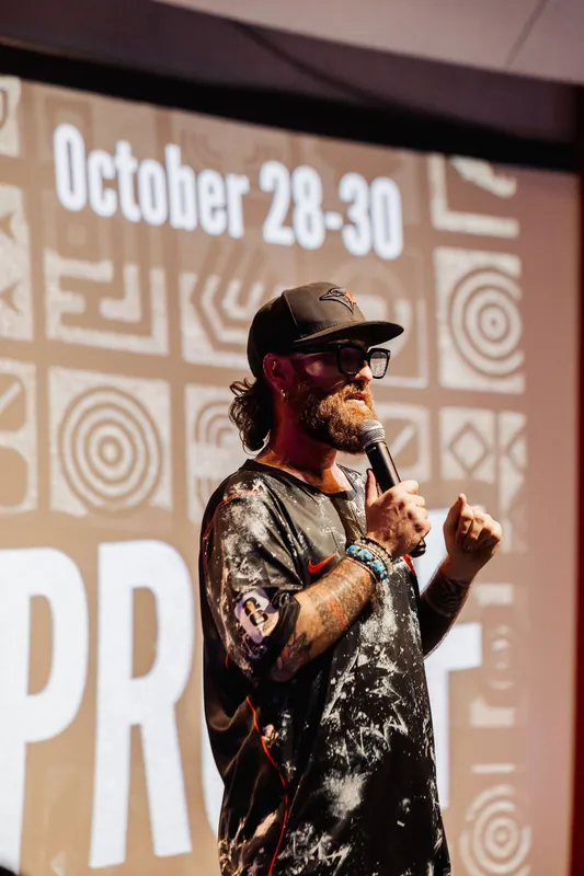 The presenter faces the room as an October 28–30 event slide looms above his shoulder, previewing a future gathering.