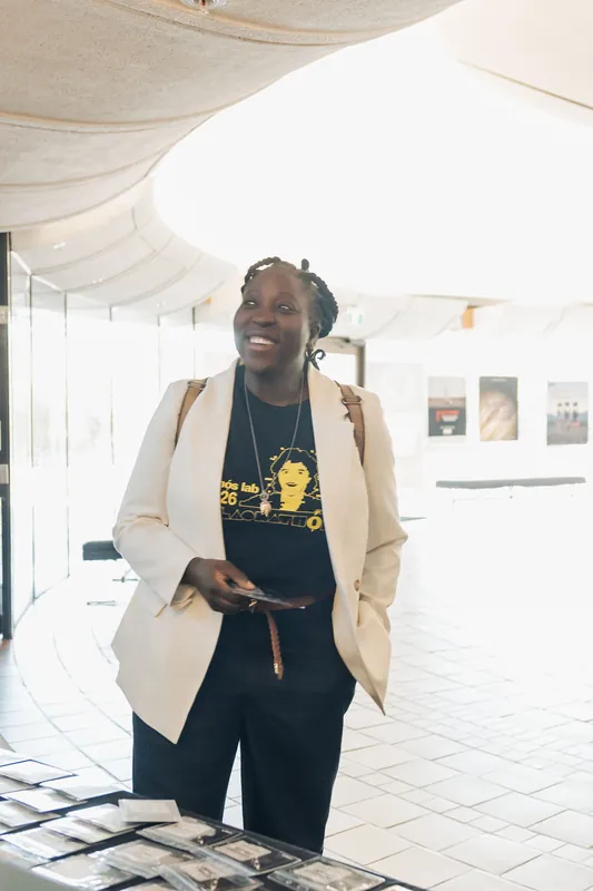 A smiling attendee in a cream blazer and Ethos Lab tee greets guests near the registration table.
