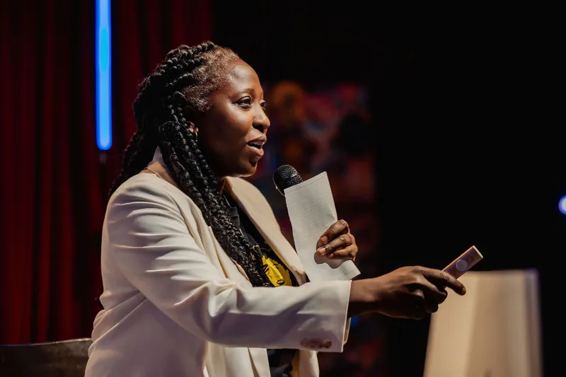 Anthonia Ogundele of Ethos Lab speaks to the crowd, notes and clicker in hand, during the indoor program.