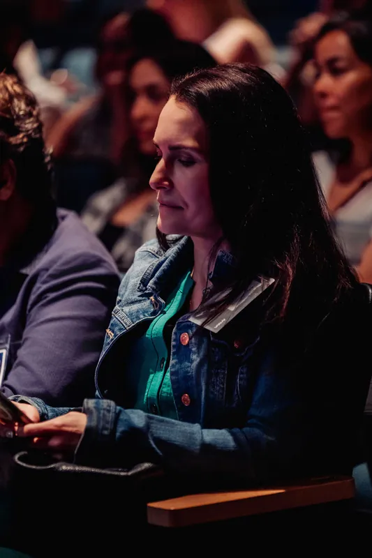 An attendee with long dark hair pauses, gaze downward, during the indoor program.