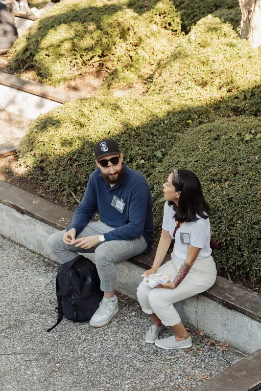 Two badge-wearing attendees sit side by side on a garden ledge deep in conversation during the pre-program reception.