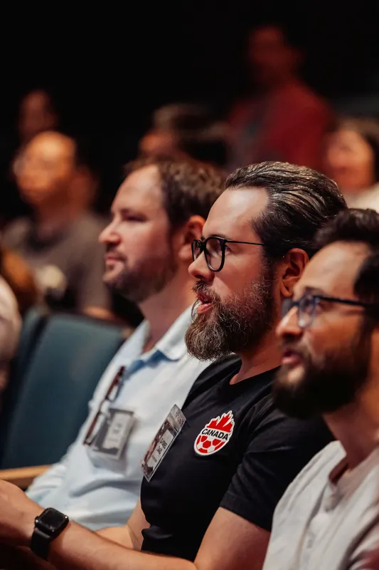 Three attendees in profile take in the stage from their theater row.