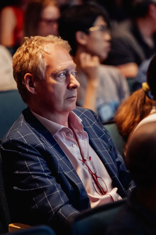An attendee in a checked blazer leans forward, caught up in the talk from his planetarium seat.
