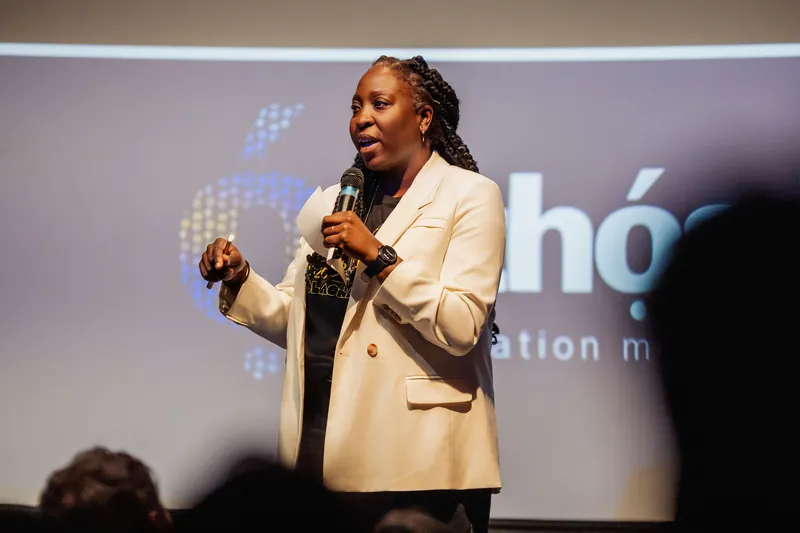 Anthonia Ogundele gestures expressively in front of the Ethos Lab logo projected on the theater screen.