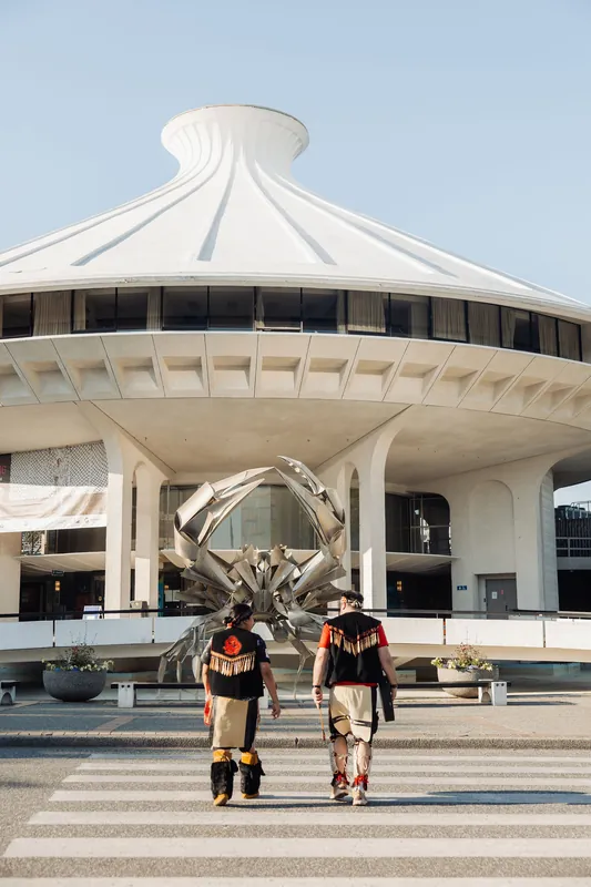 A slightly wider angle captures both performers mid-stride with the Space Centre's full dome and sculpture rising behind them.