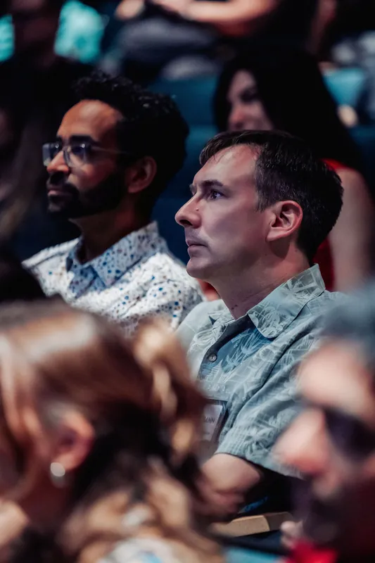 Two attendees sit side by side, fixed on the unfolding action on stage.