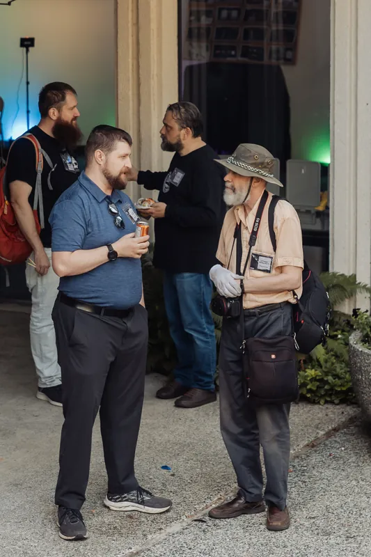 Two guests talk near the Space Centre entrance — one with a camera bag and safari hat, the other holding a drink — as the program sets up inside.