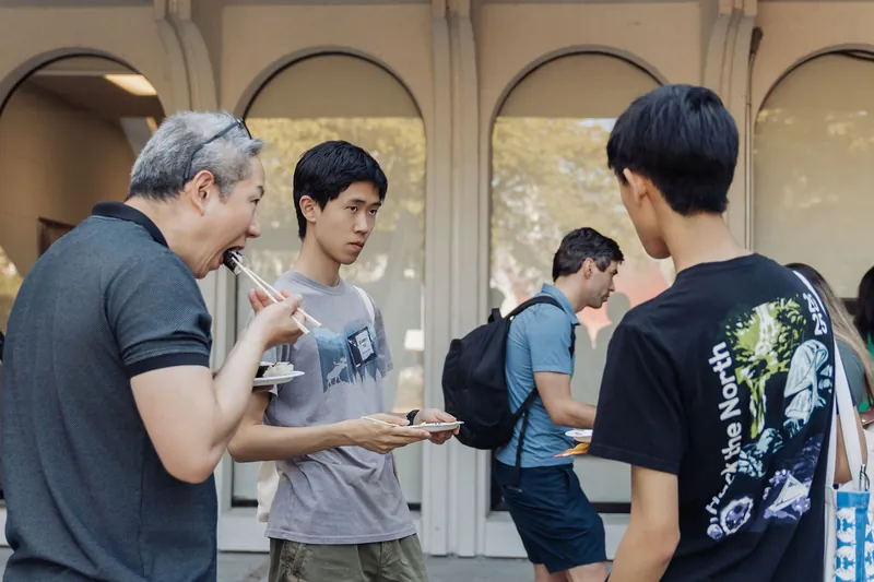 Three attendees enjoy sushi with chopsticks and easy conversation on the outdoor plaza before the program.