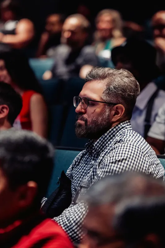 A bearded attendee in a plaid shirt watches the talks from his seat.
